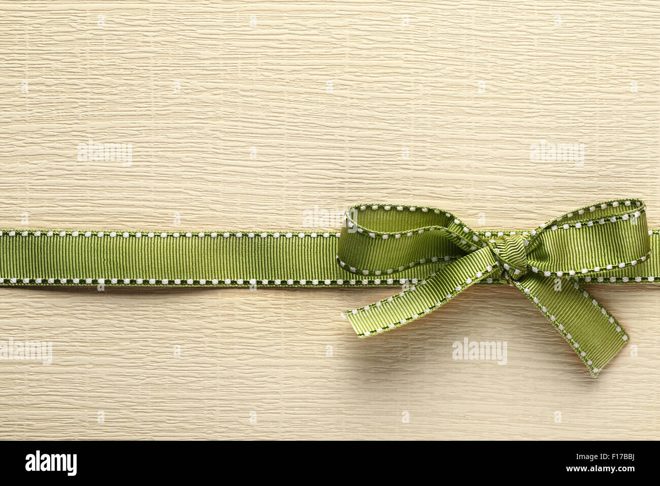 Green ribbon bow on golden paper textured  background Stock Photo