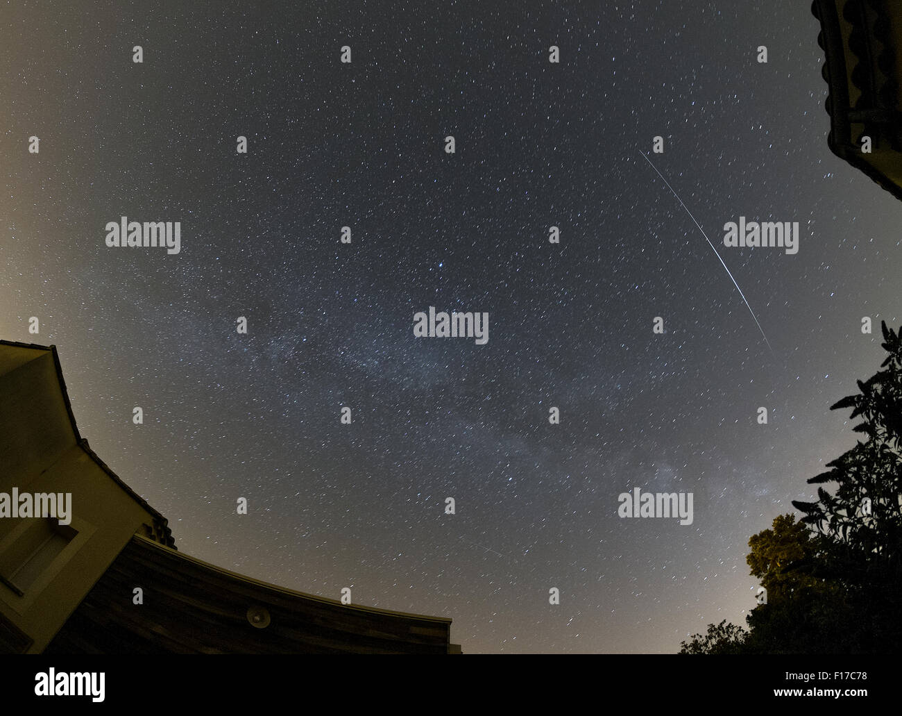 A satellite flares in the night sky with stars of the Milky Way Stock Photo