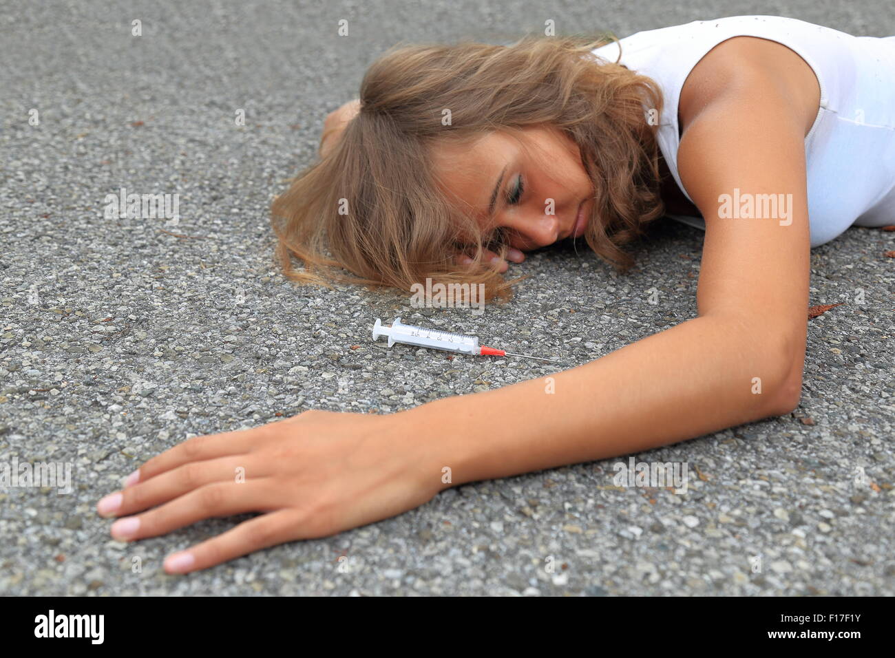 A Drug-addicted Teenager wirh syringe lying on a street Stock Photo