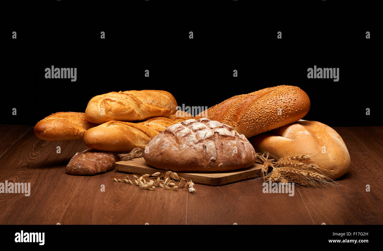 Different bread and wheat on dark wooden table background Stock Photo ...