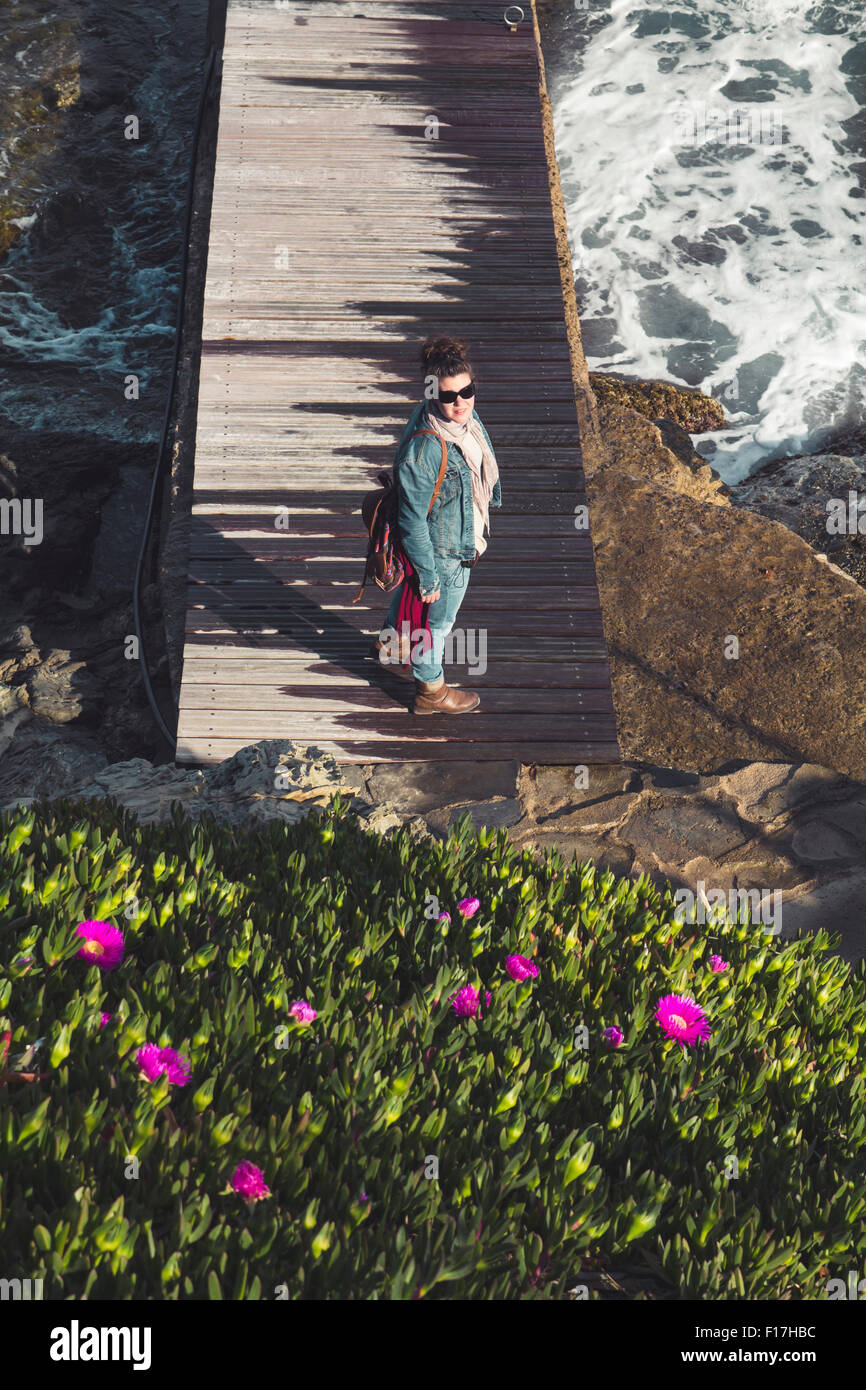 Woman standing in a wood pier, with purple flowers Stock Photo