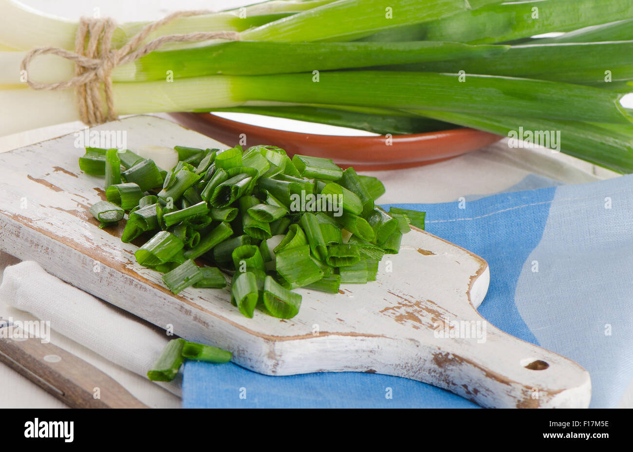Chopped green onions on a white wooden cutting board. Selective focus ...