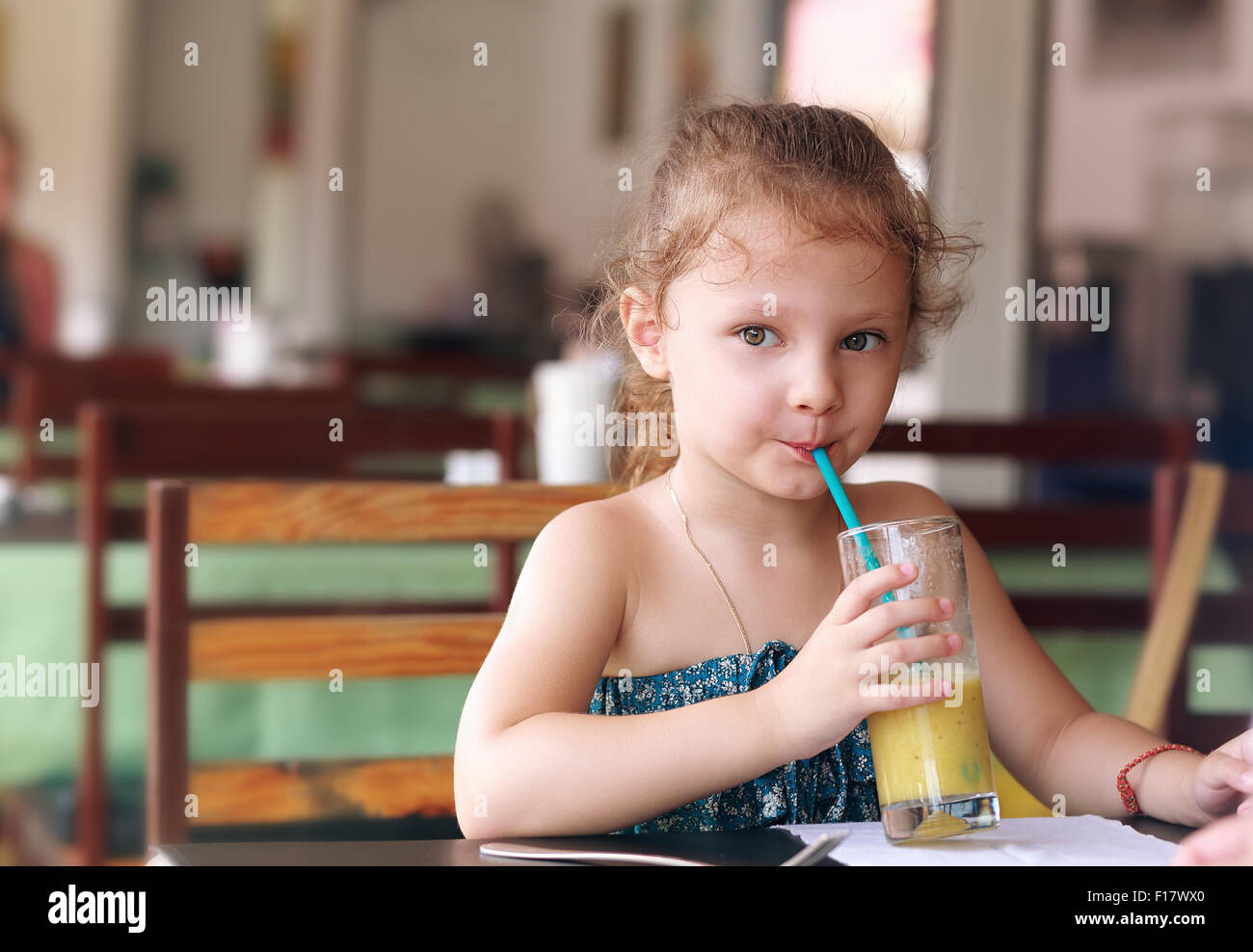 Cute small kid girl drinking juice in cafe with serious look Stock Photo