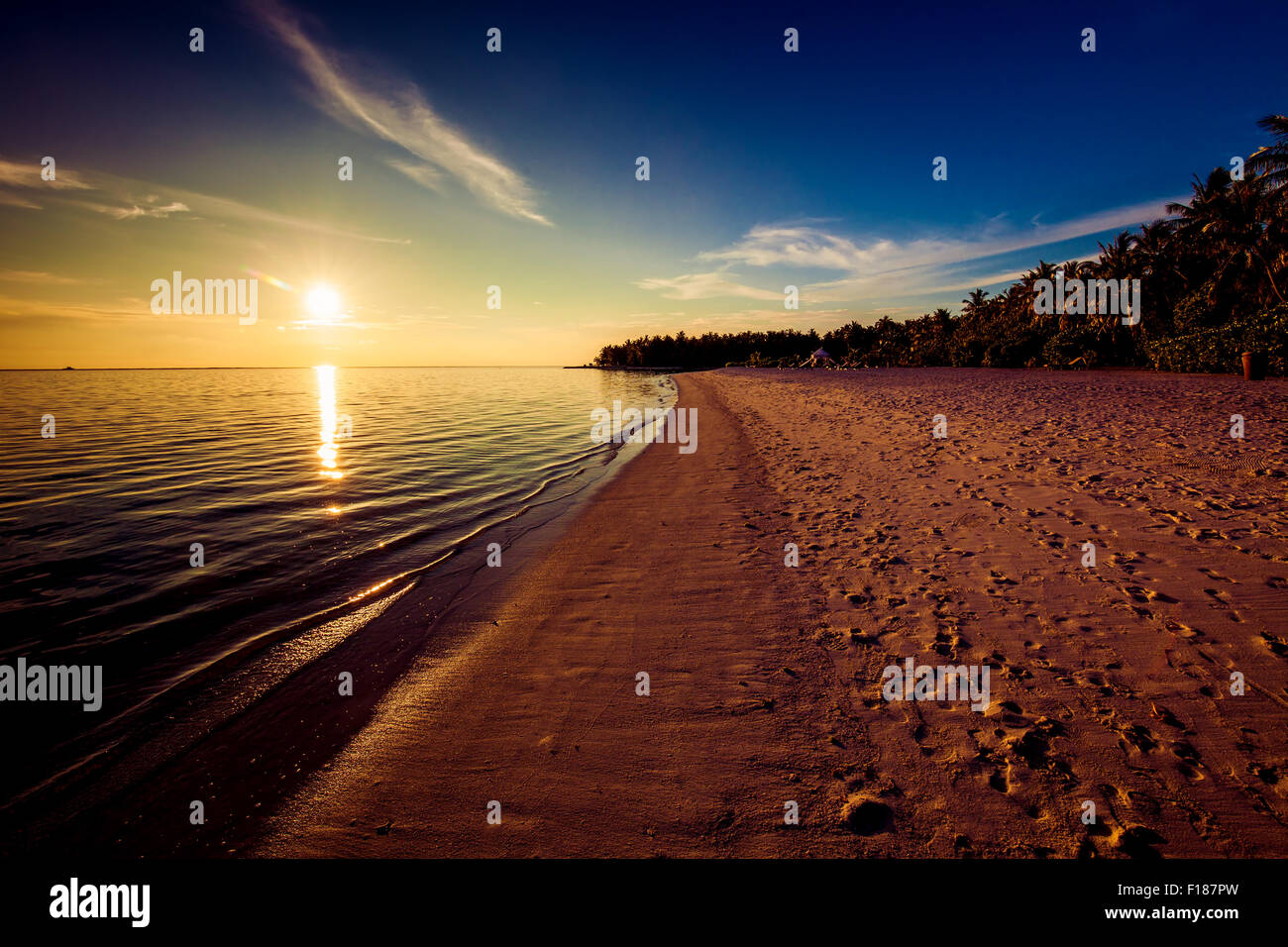 Footprints on the tropical beach at sunset with sun over ocean Stock Photo