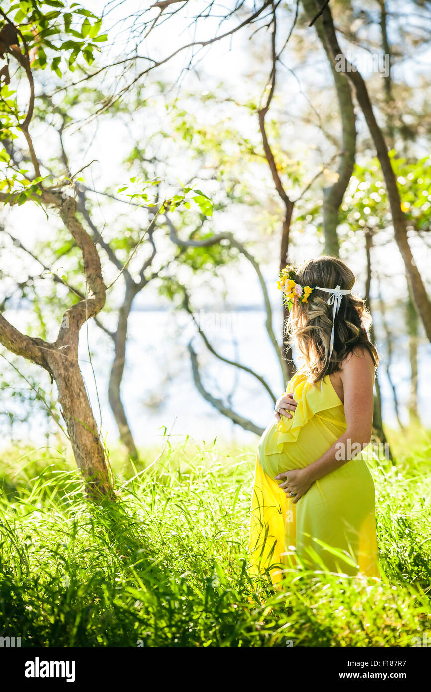 Profile view of pregnant woman with long hair in yellow dress in the park Stock Photo