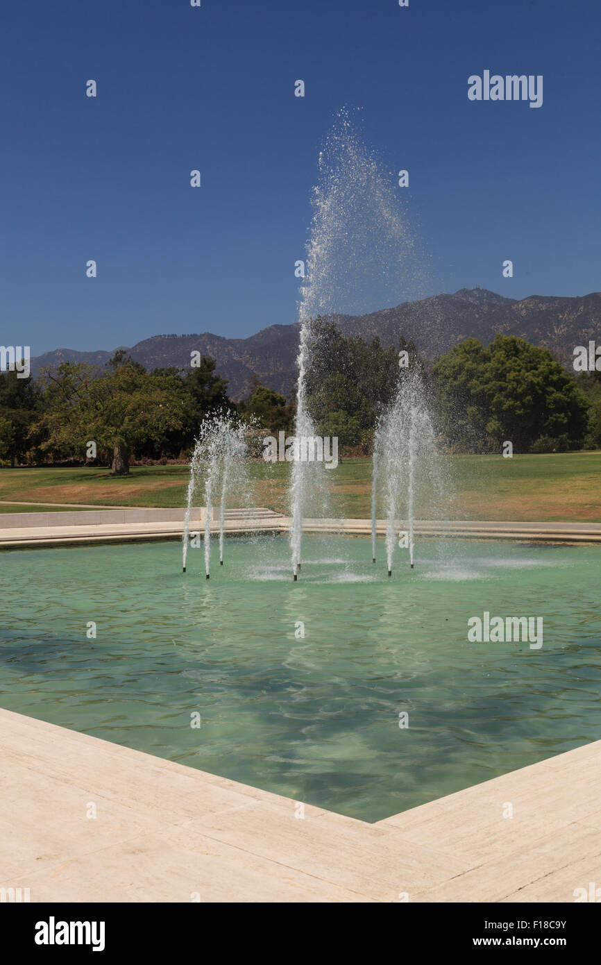 Blue spraying fountain of water with the mountains in the background at Los Angeles Arboretum gardens in California, United Stat Stock Photo