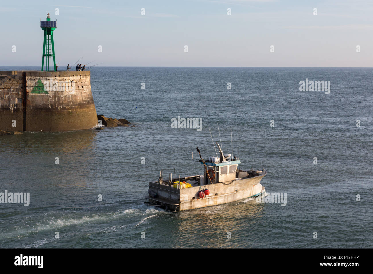 A fishing boat heads out to sea past anglers on the harbour wall at Port-en-Bessin, Normandy, France Stock Photo