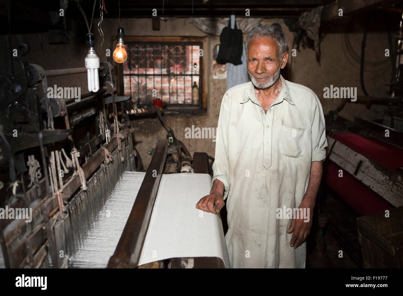India, Jammu & Kashmir, Srinagar, pashmina production, man weaving pasminas on mechanical loom in dark workshop Stock Photo