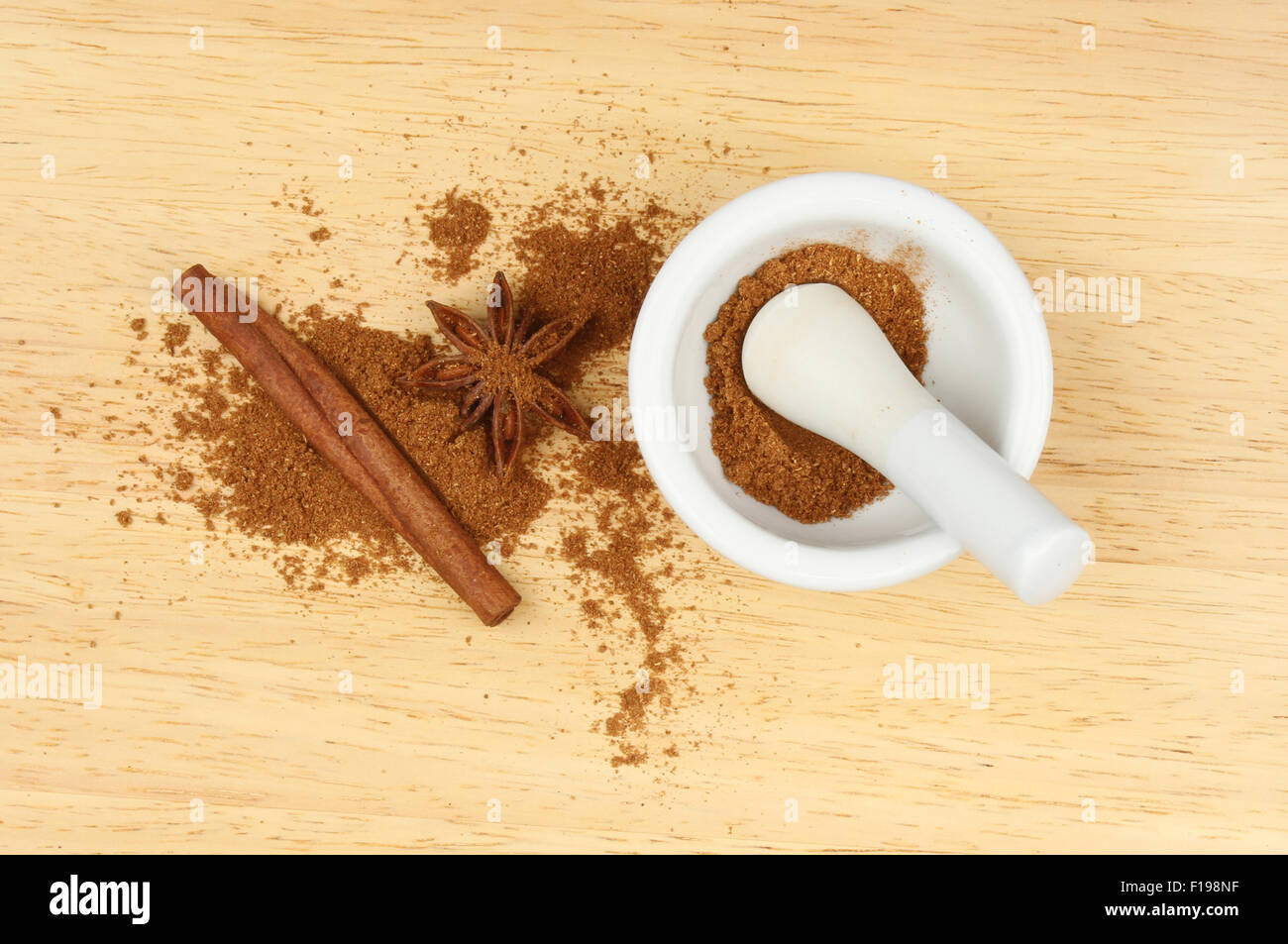 Chinese five spice in a pestle and mortar with star anise and cinnamon on a wooden board Stock Photo