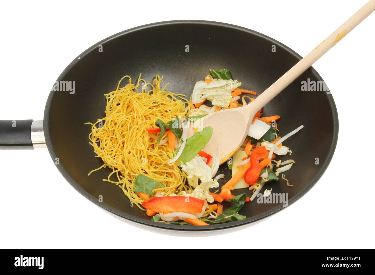 Closeup of a wok with stir fry vegetables and noodles with a wooden spoon isolated against white Stock Photo