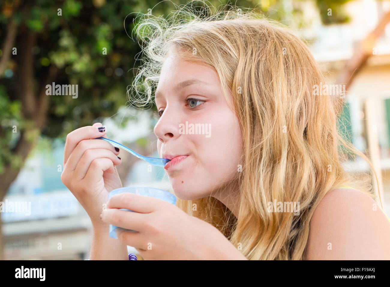 Blond Caucasian teenage girl eats frozen yogurt, closeup outdoor portrait with natural light Stock Photo
