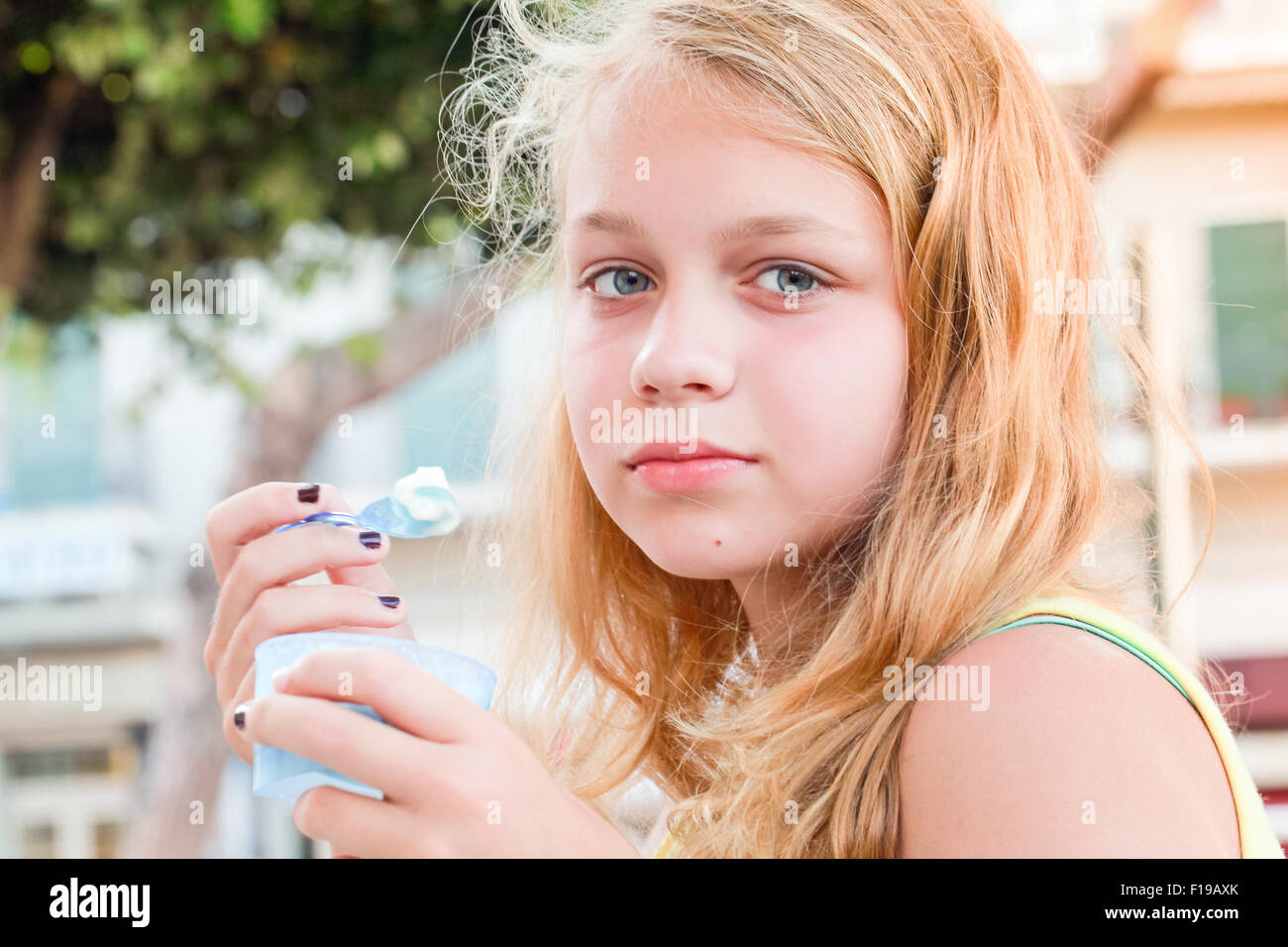 Blond Caucasian teenage girl with frozen yogurt, closeup outdoor portrait with natural light Stock Photo