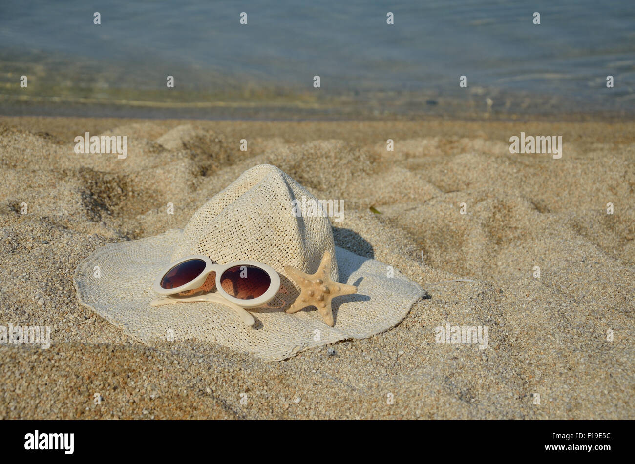 Straw hat, glasses and sea star set on a beach with sea in background ...