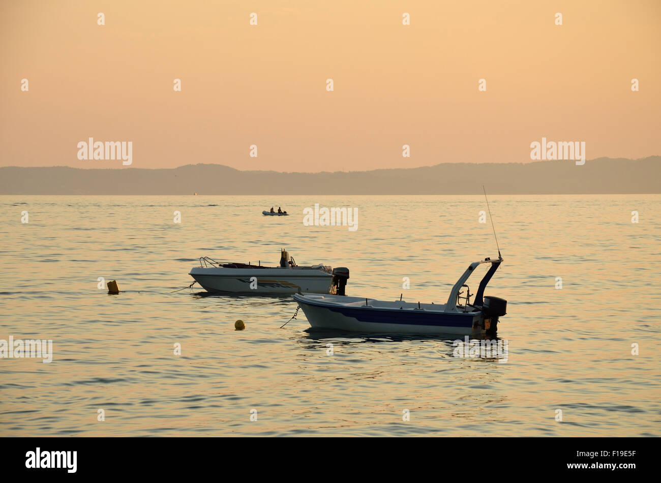 Two boats on sea with a third one and mountains in background in sunset time Stock Photo