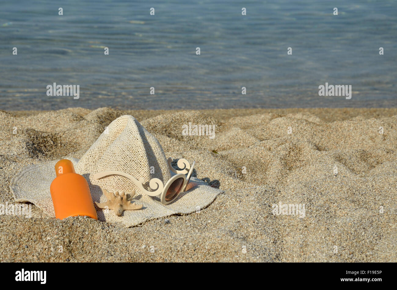 Straw hat, sun lotion, glasses and sea star set on a beach with sea in ...