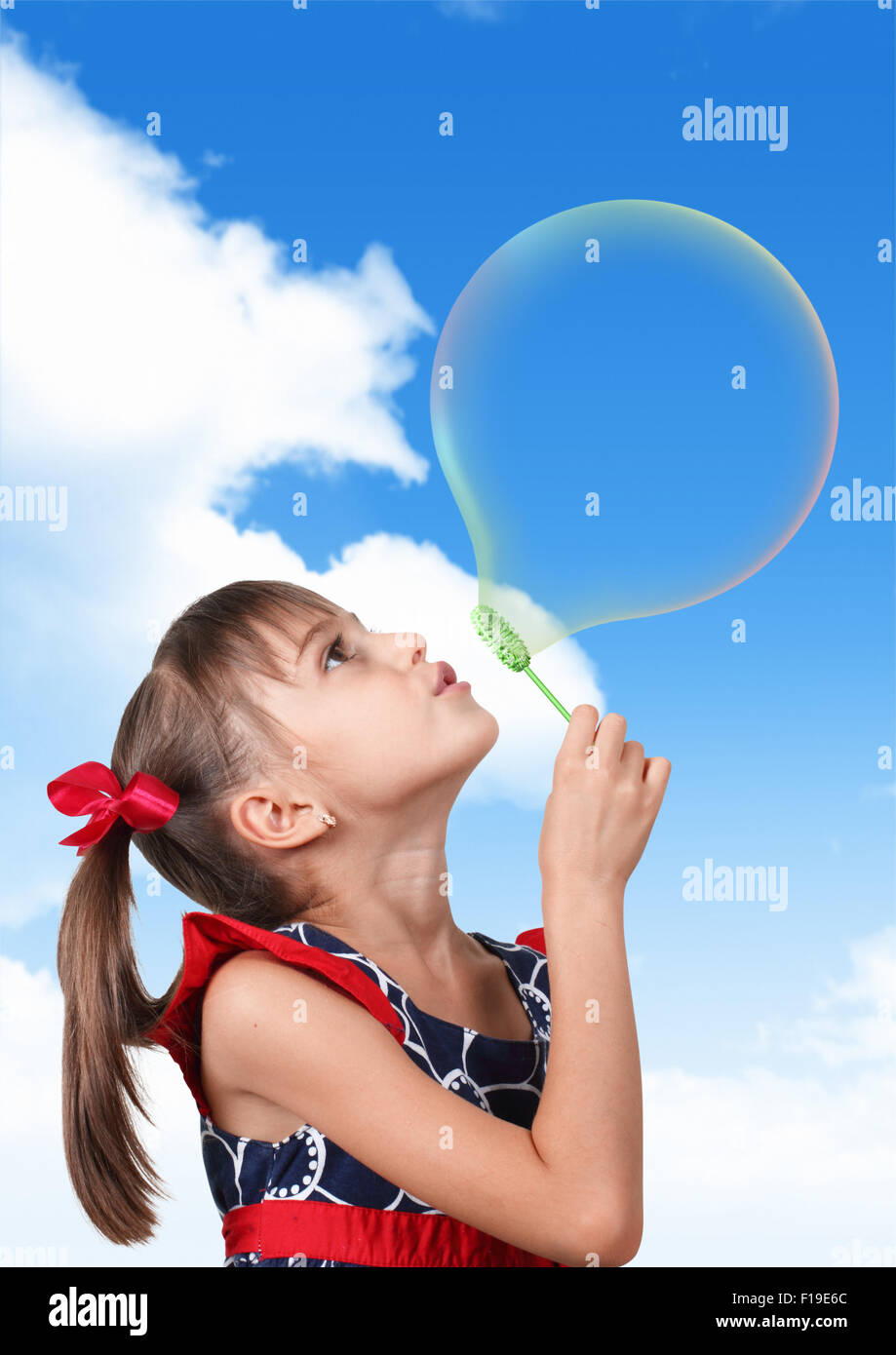Portrait of funny child girl blowing big soap bubble on blue sky background Stock Photo