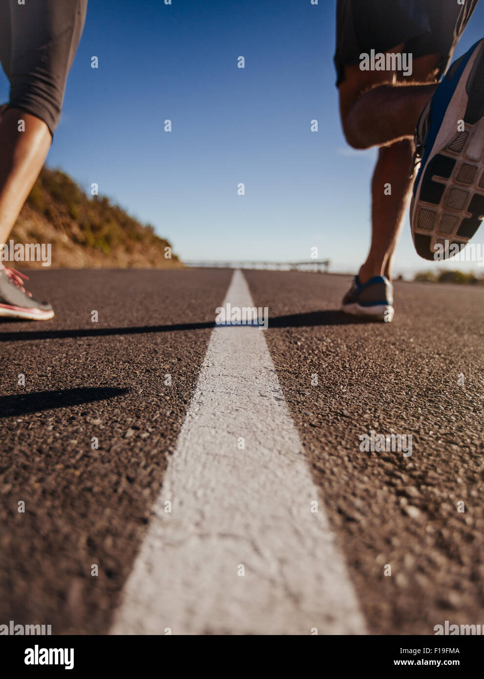 Low angle shot of runners legs running on middle of the road. Rear view