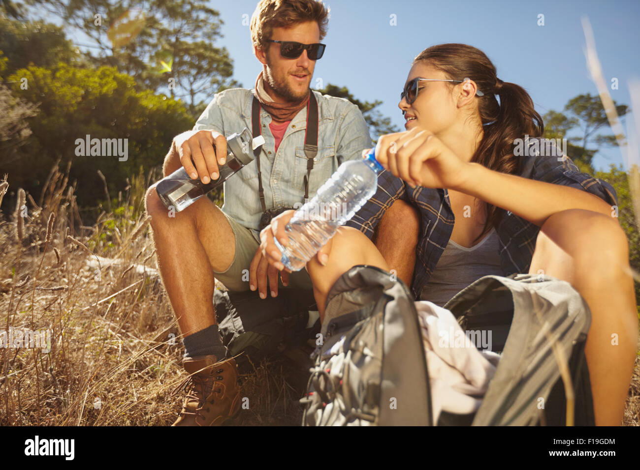 Young couple taking a break on a hike. Caucasian man and woman drinking water while out hiking Stock Photo