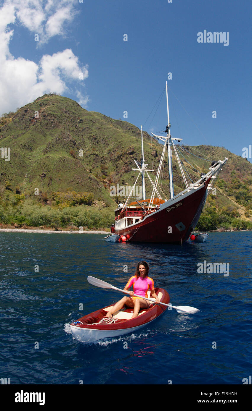 px91346-D. woman (model released) kayaks along Sangeang Island's verdant shores between scuba dives from the Seven Seas live-abo Stock Photo