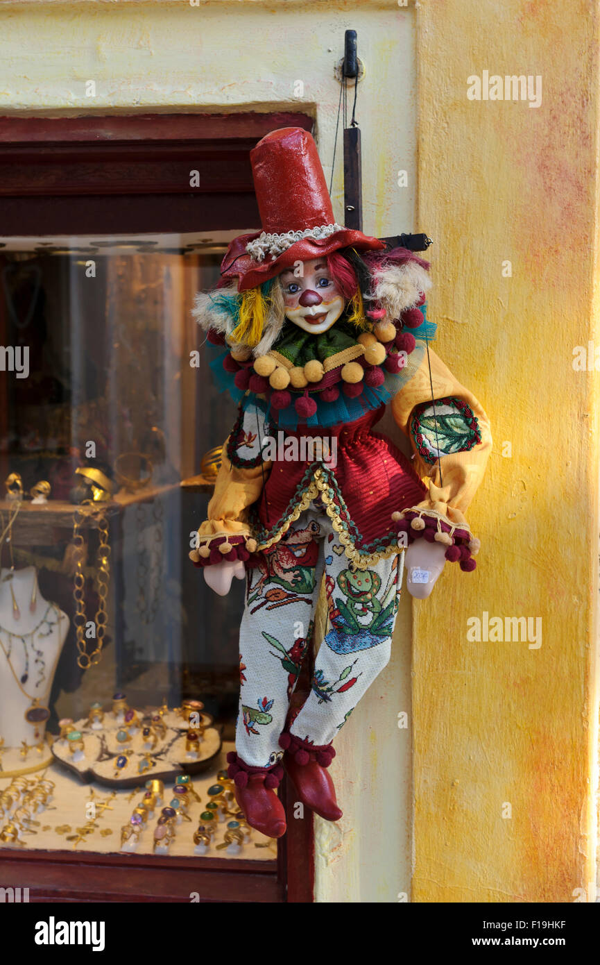A colourful clown puppet hanging on strings outside a shop window in