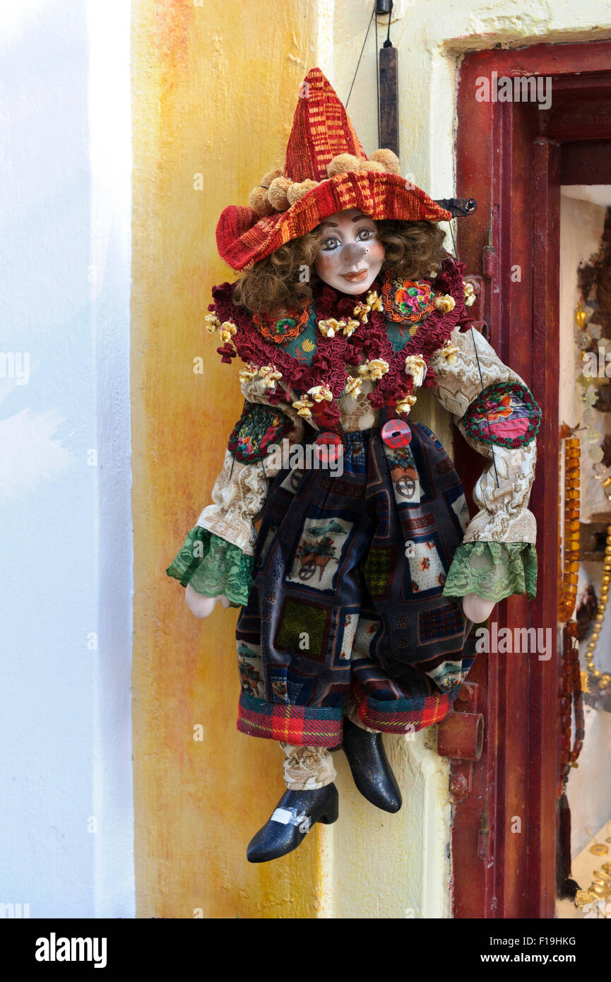 A colourful clown puppet hanging on strings outside a shop window in