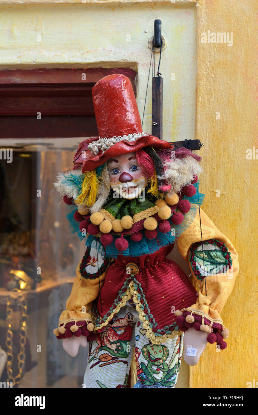 A colourful clown puppet hanging on strings outside a shop window in