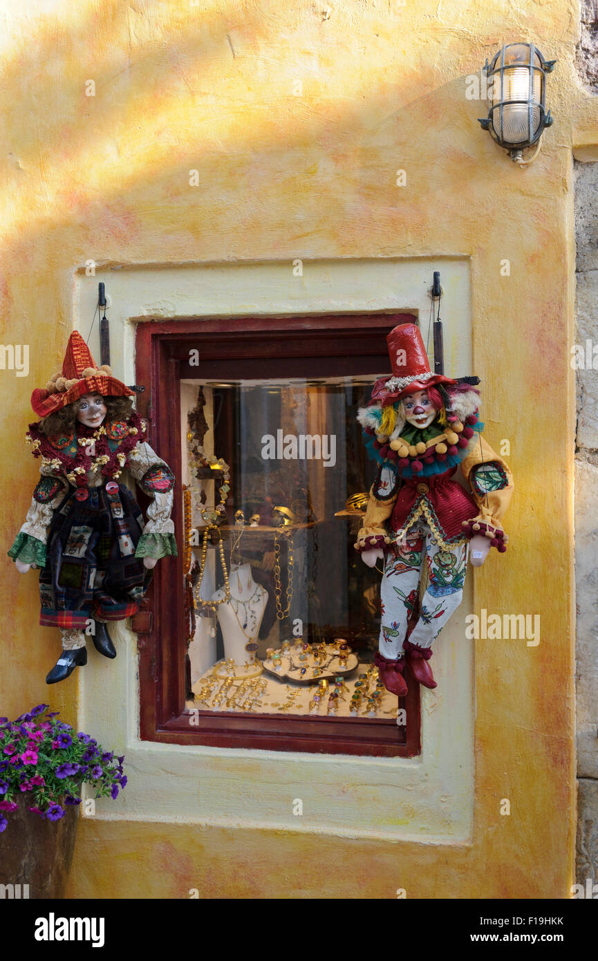 Two colourful clown puppets hanging on strings outside a shop window in