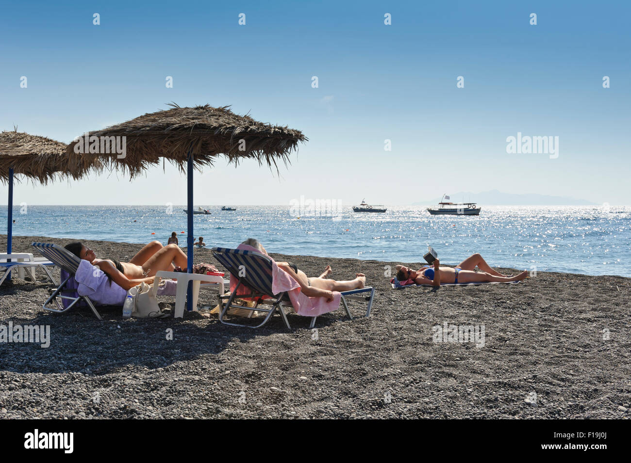 Three female sunbathers on Kamari beach, Santorini, Greece. Stock Photo