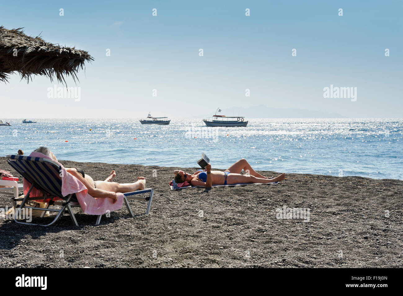 Two female sunbathers on Kamari beach, Santorini, Greece. Stock Photo