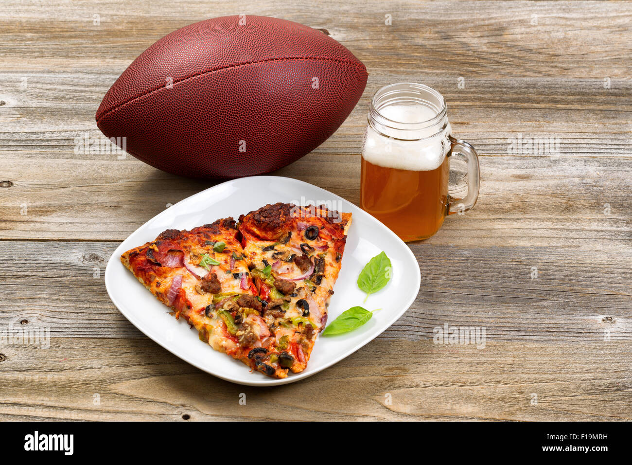 Two slices of freshly baked pizza in a white plate, football, and a pint of justly poured beer setting on rustic wooden table. Stock Photo