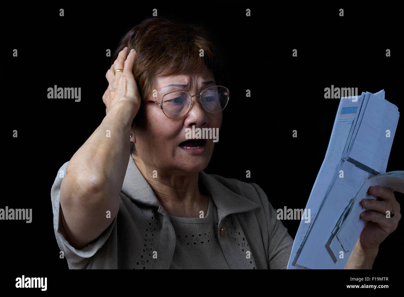 Senior woman stressed out by looking at her bills. Black background. Stock Photo