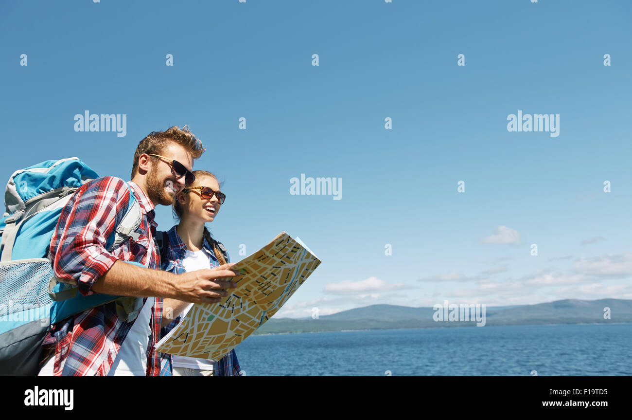 Happy hikers in sunglasses looking in guide on background of the sea Stock Photo