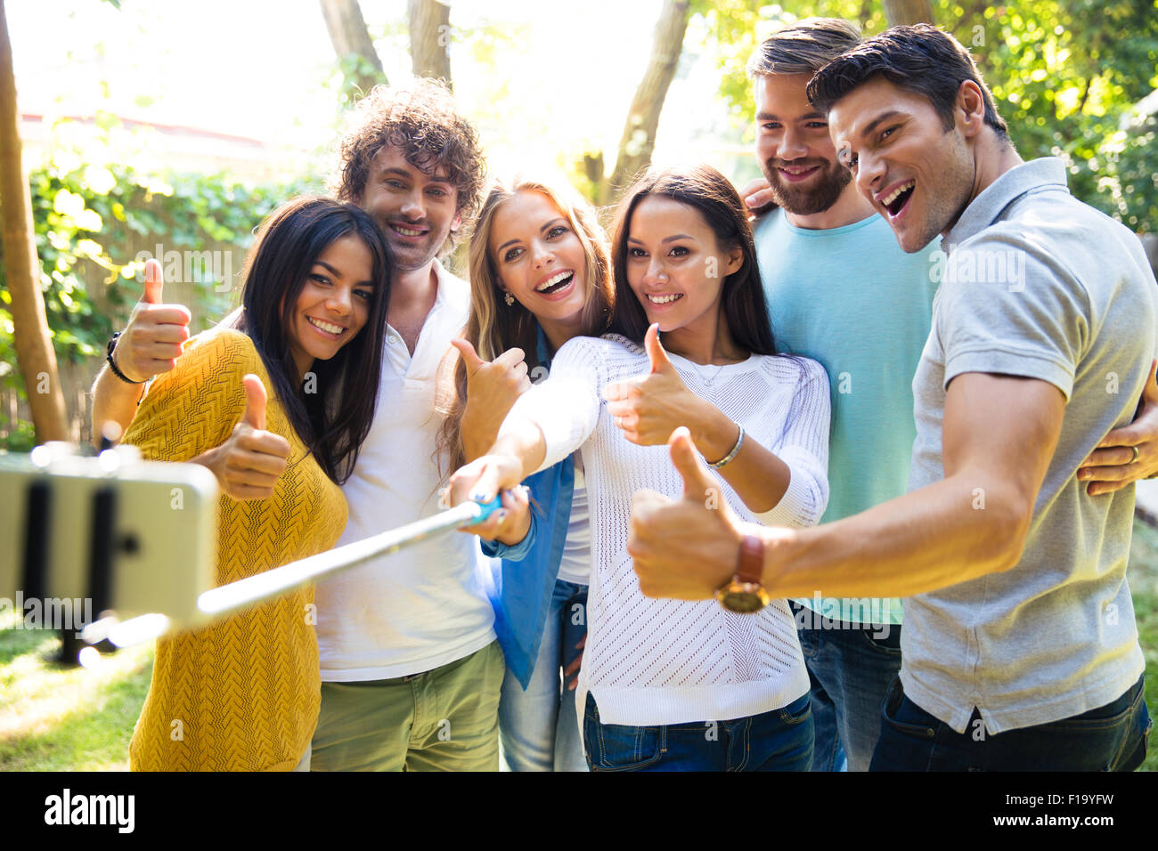 Happy friends making selfie photo on smartphone while showing thumbs up outdoors Stock Photo