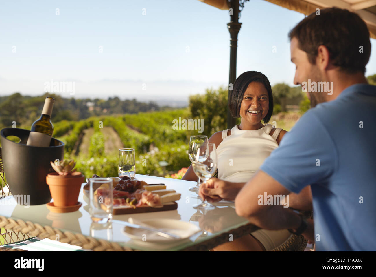 Happy young couple at winery restaurant with vineyard in background. Smiling young woman with a man sitting at table drinking wi Stock Photo