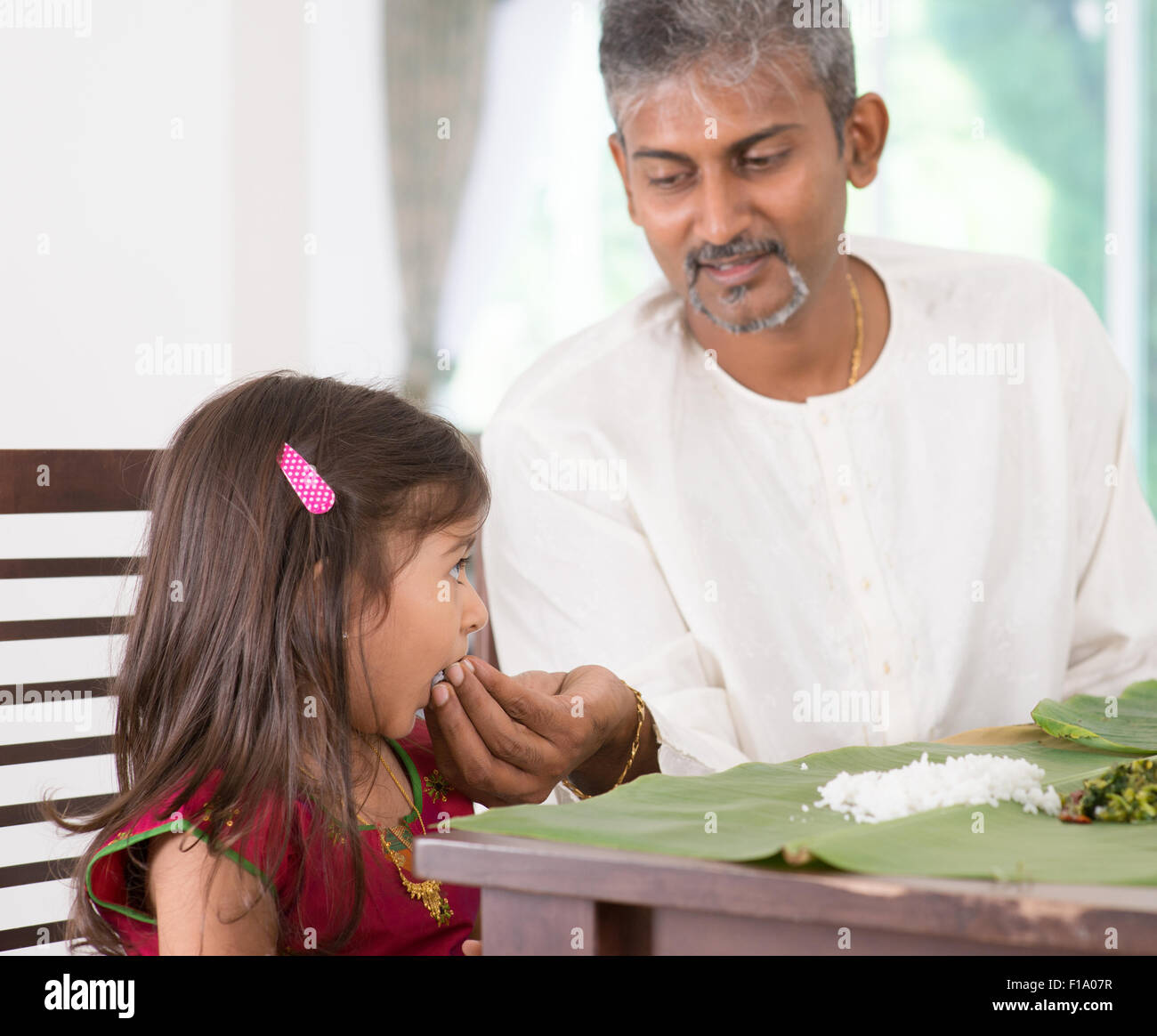 Indian family dining at home. Candid photo of India people eating rice with hands. Parent feeding child. Stock Photo