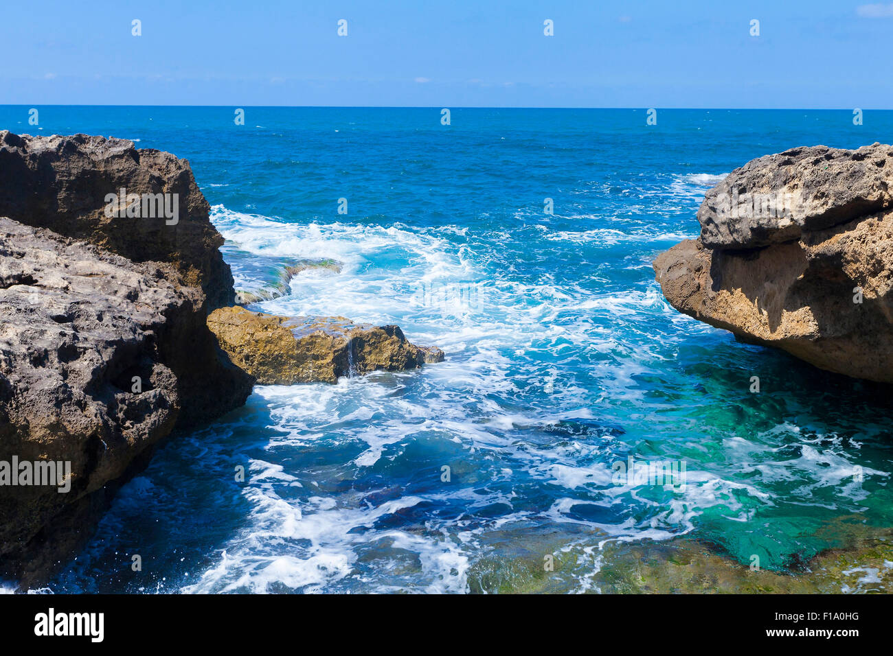 Foamy waves between huge rocks facing smooth horizon line Stock Photo ...