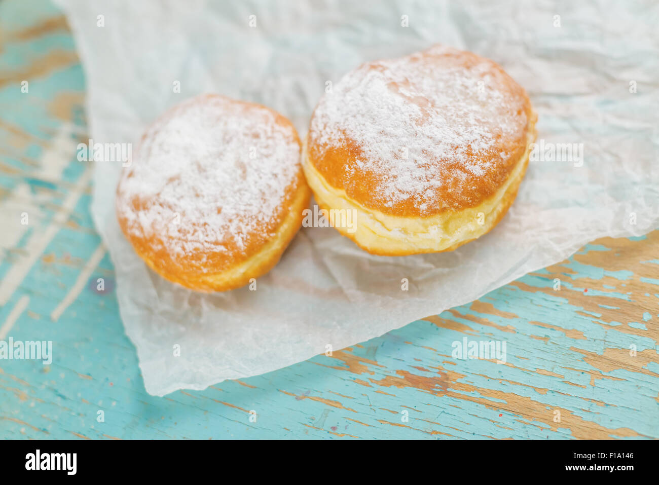 Sweet sugary donuts on rustic wooden kitchen table, tasty bakery doughnuts on crumpled baking paper in vintage retro toned image Stock Photo