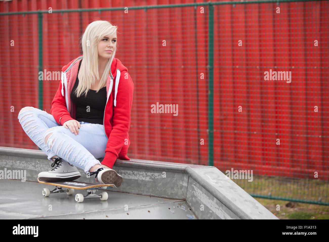 Pretty teenage girl sitting down outside with feet on skateboard at a skate park. Stock Photo