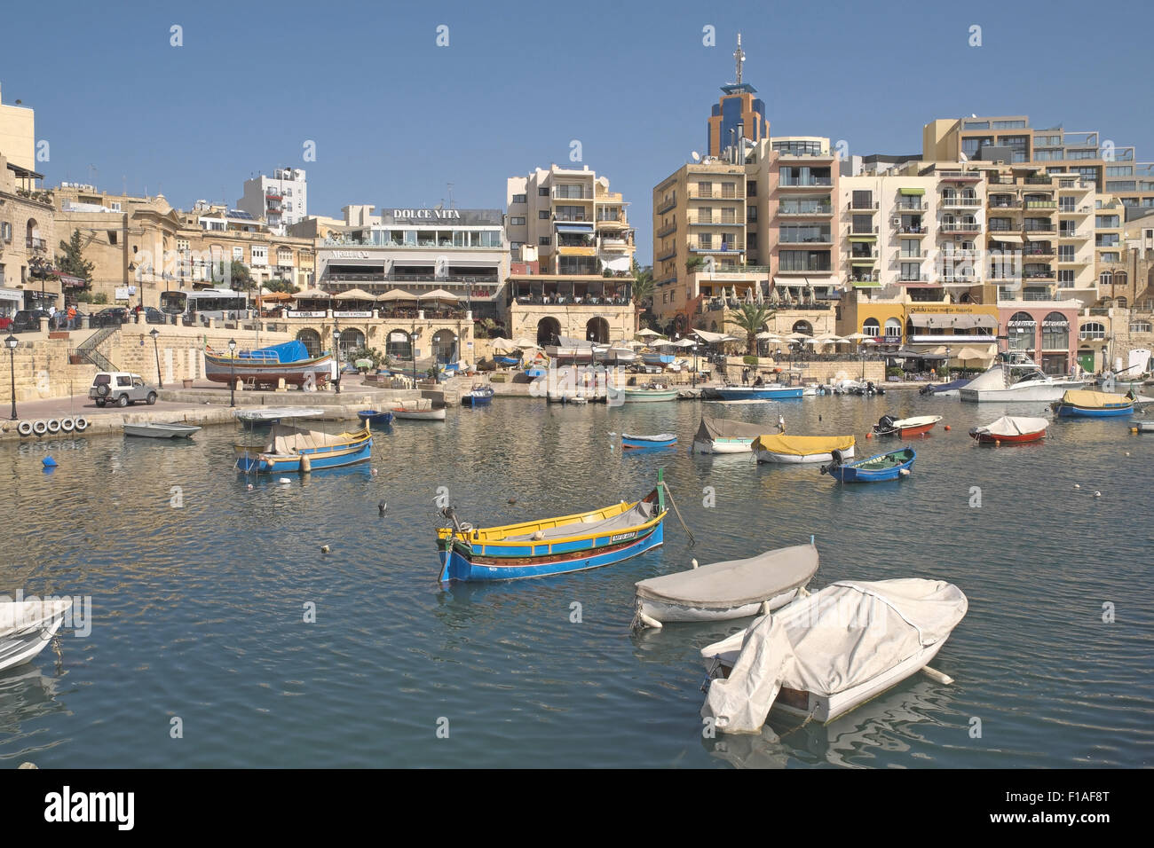 Brightly painted traditional fishing boats with stone buildings beyond, St Julian's Bay, Malta. Stock Photo