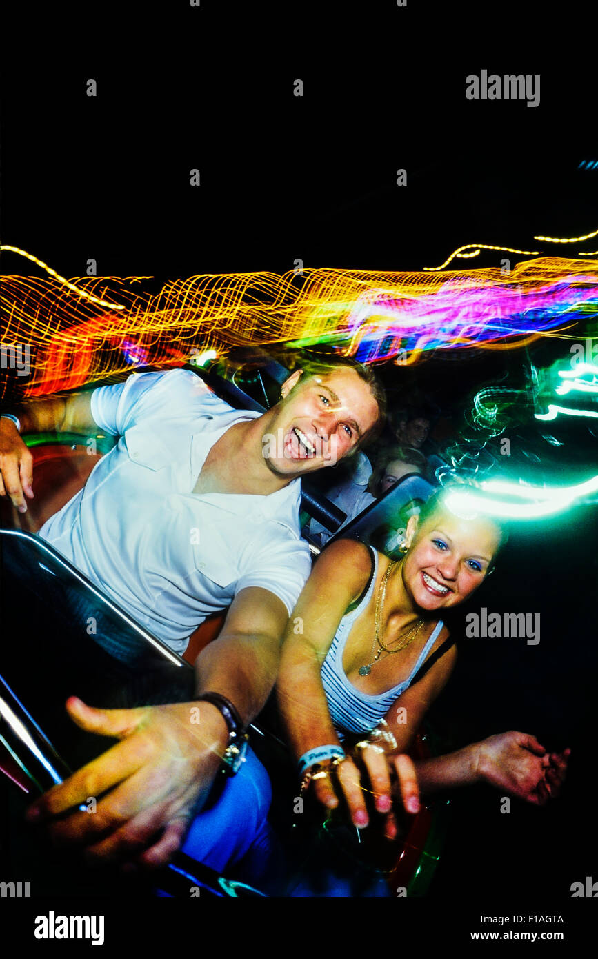 A young adult couple enjoying a roller coaster ride at night at