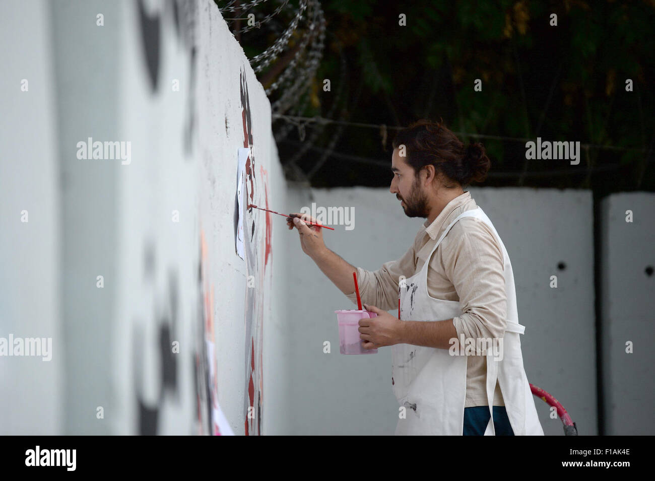Civil society activist Omaid Sharifi paints graffiti on a cement blast wall in Kabul (Afghanistan), 15 August 2015). They are part of the self-style 'Artlords of Kabul,' a mixed-bag of artists and activists on a mission to claim their city back, by adorning the high security walls across Kabul with eye-catching graffiti images and simple messages. The artwork, titled an ordinary hero - the hero of my city, is a tribute to street sweepers on the wall that protects the Afghan Central Bank building. So far, the group has painted outside the presidential palace, as well as the headquarters of nati Stock Photo