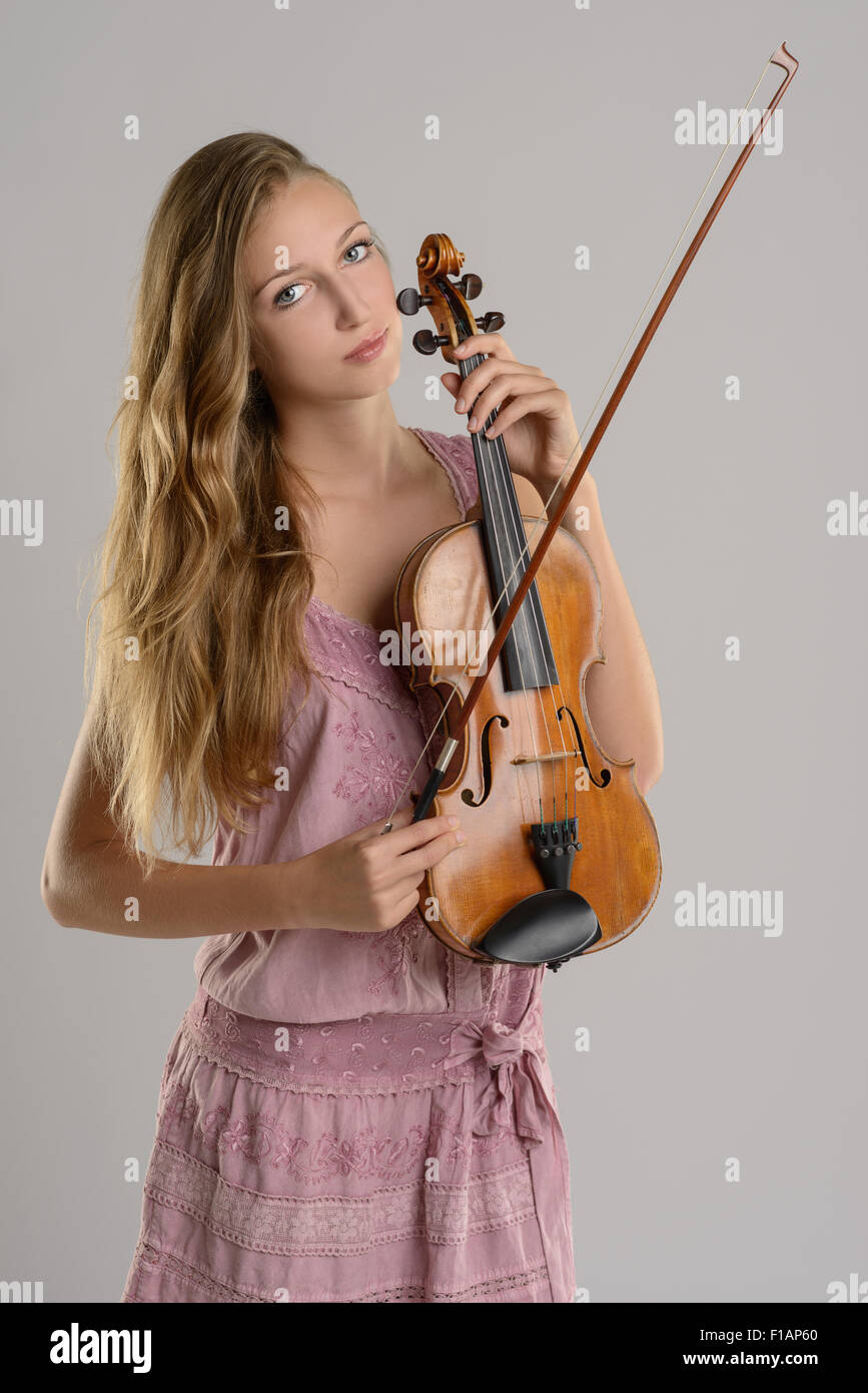 Attractive young female musician standing holding her violin cradled in her arm while looking at the camera with a smile, over a Stock Photo