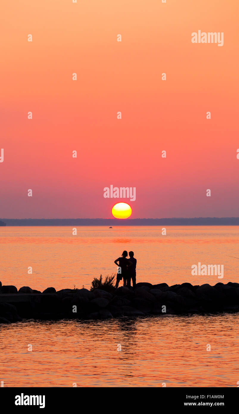 People silhouetted against a vibrant sky as the sun sets over Lake Simcoe. Willow Beach, Ontario, Canada. Stock Photo