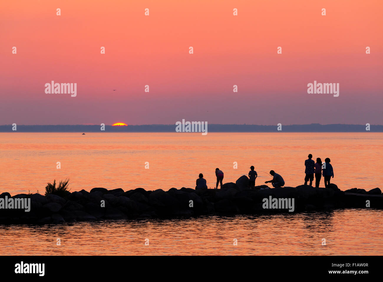People silhouetted against a vibrant sky as the sun sets over Lake Simcoe. Willow Beach, Ontario, Canada. Stock Photo