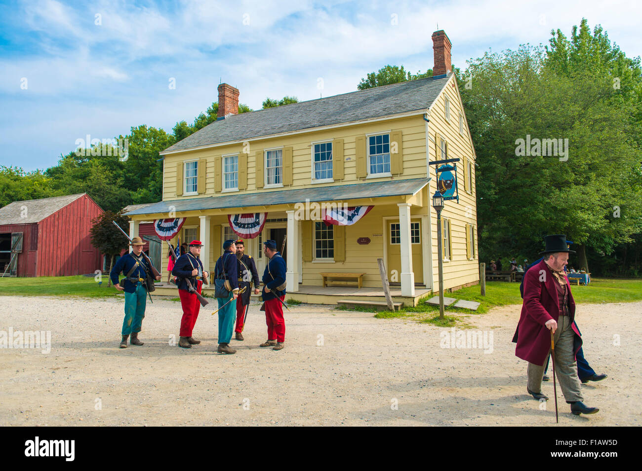Old Bethpage, New York, USA. 30th August, 2015. A 19th Century gentleman wearing a top hat, and American Civil War soldiers from the 14th Brooklyn Regiment (14th New York State Militia) AKA The Brooklyn Chasseurs, are portrayed in front of the yellow Noon Inn tavern during the Old Time Music Weekend at the Old Bethpage Village Restoration. During their historical reenactments, members of the non-profit 14th Brooklyn Company E wear reproductions of 'The 'Red Legged Devils' original Union army uniform. Credit:  Ann E Parry/Alamy Live News Stock Photo