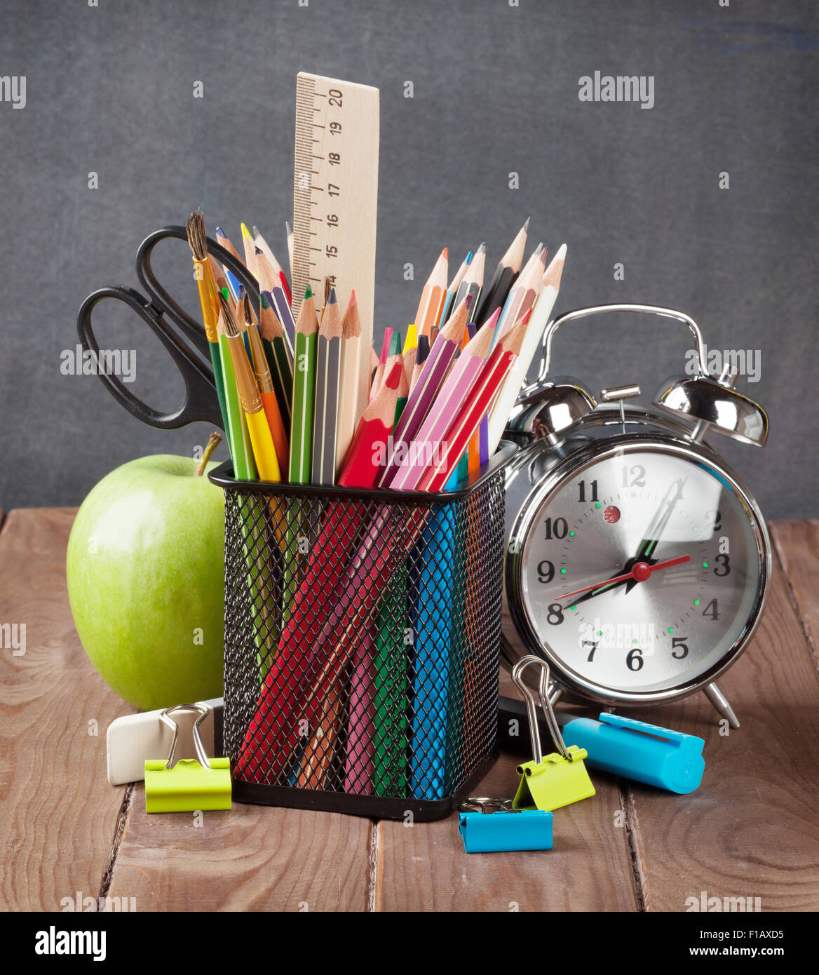 School and office supplies, alarm clock and apple on classroom table Stock Photo