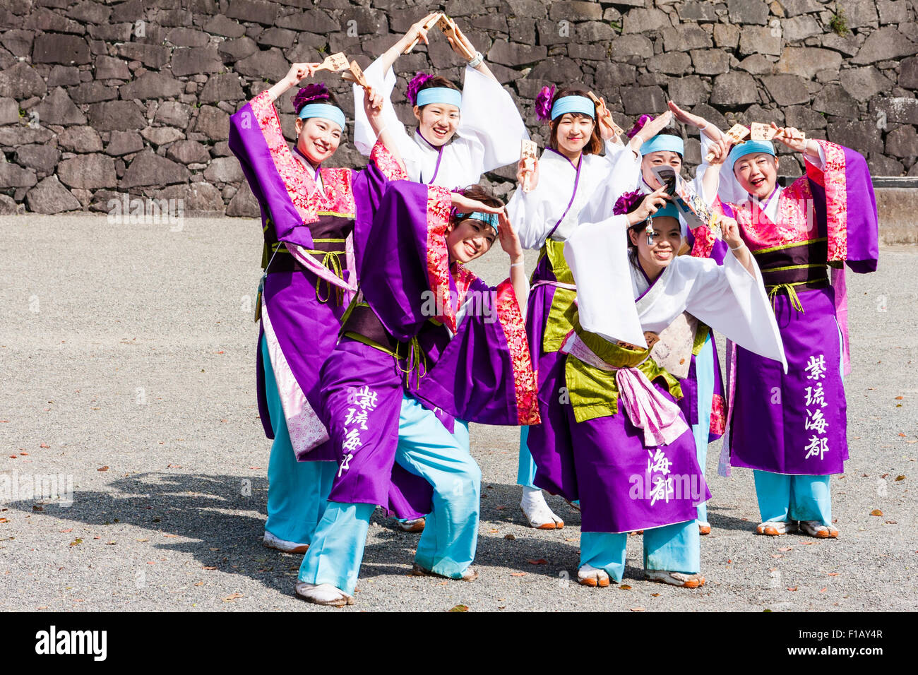 Japanese yosakoi dance team of smiling young women posing for photograph with their arms raised in front of Kumamoto castle stone wall. Stock Photo
