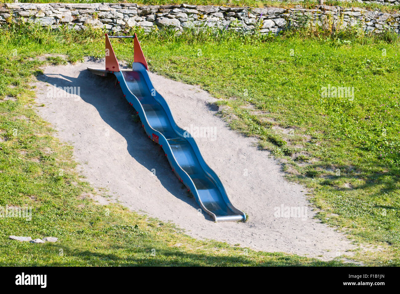 Long Blue and red Metal wavy slide on a grass slope of a playground