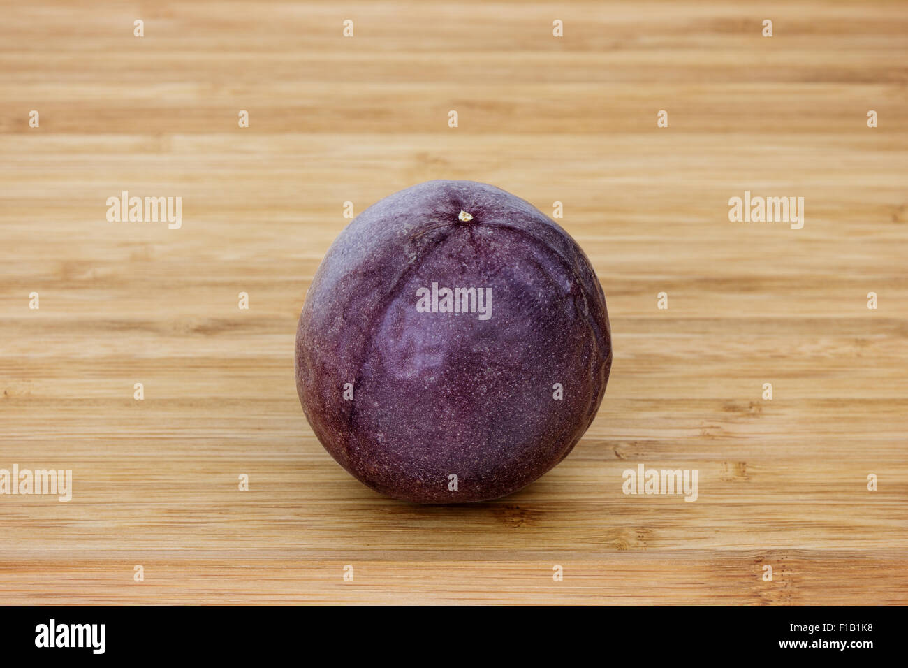 Close-up of a whole passion fruit (passionfruit, purple granadilla (Passiflora edulis)) on a wooden table. Stock Photo