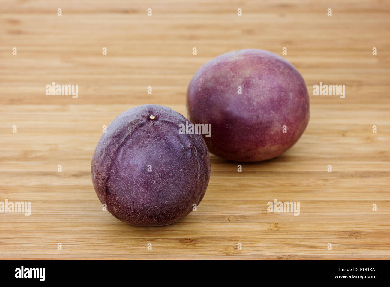 Close-up of two whole passion fruits (passionfruit, purple granadilla (Passiflora edulis)) on a wooden table. Stock Photo